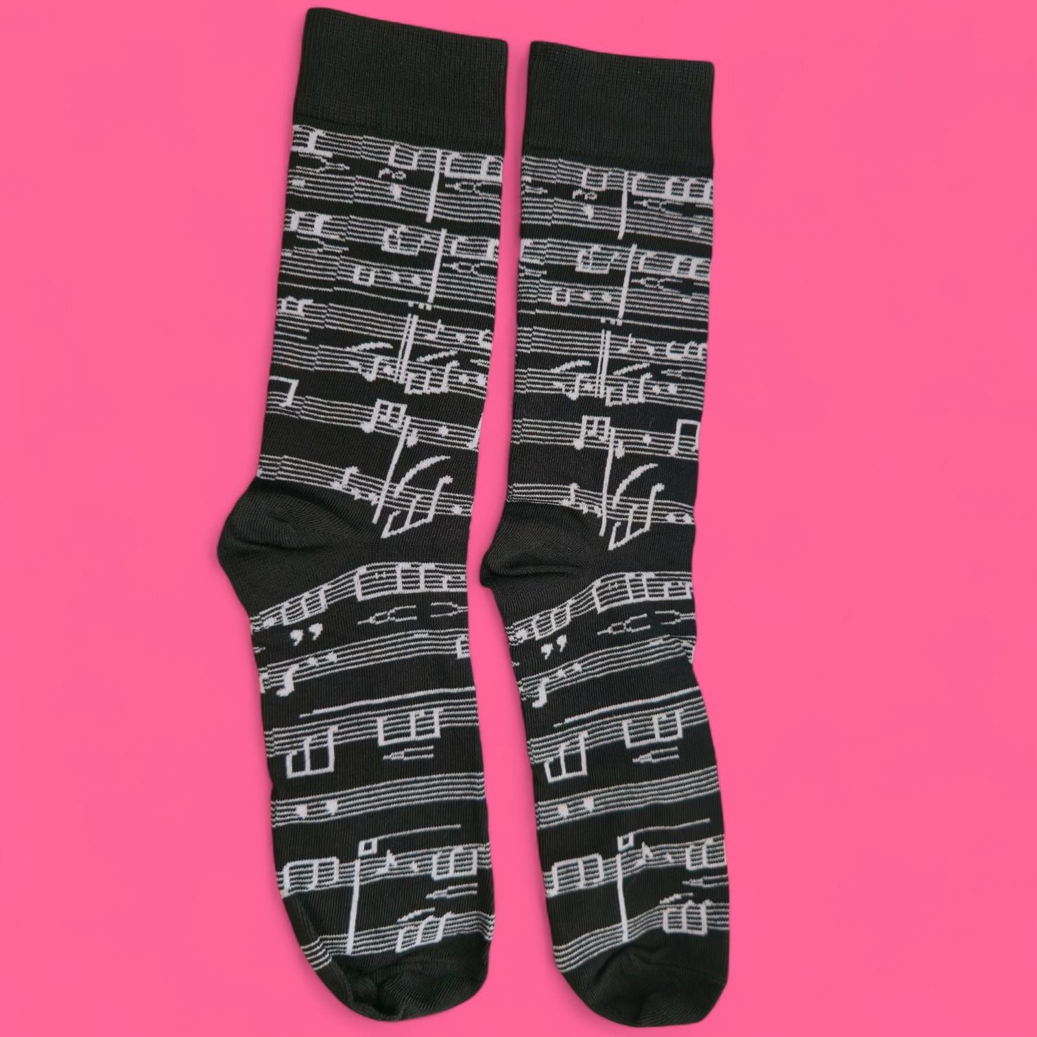 Calcetines negros con notas musicales y símbolos blancos sobre fondo rosa.