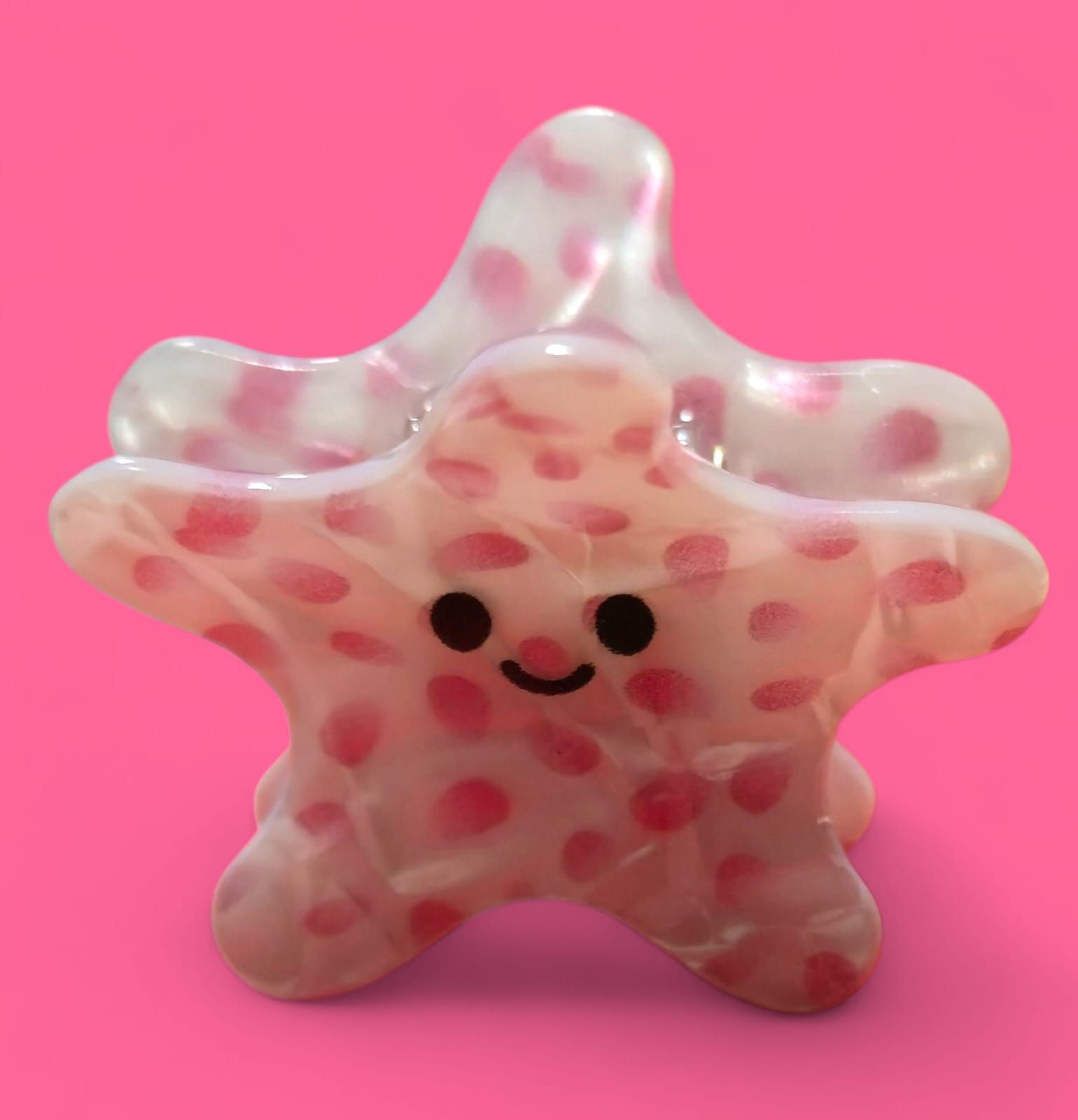 Dos figuritas en forma de estrella, con lunares rosas y caras sonrientes. Una está encima de la otra sobre un fondo rosa.