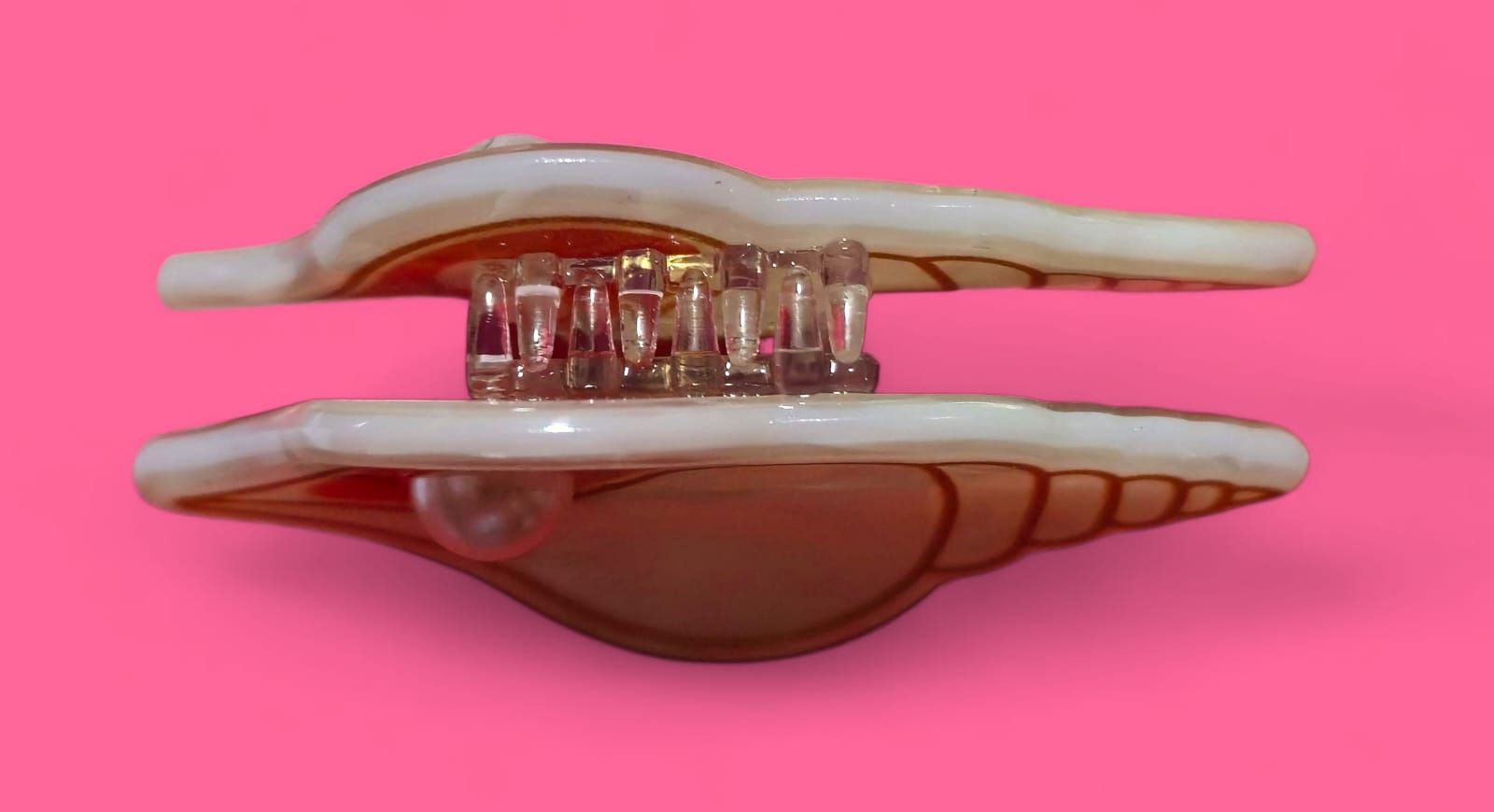 Caja de baratijas con forma de concha de almeja y detalle de perlas, sobre fondo rosa.