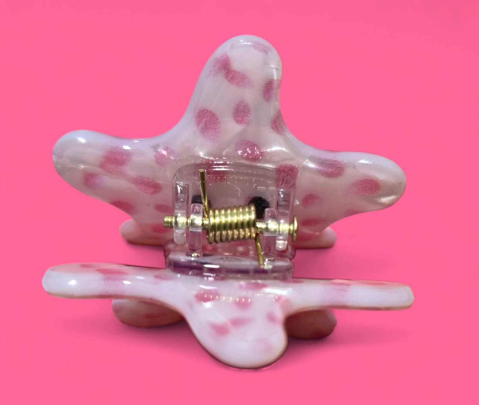 Dos figuritas en forma de estrella, con lunares rosas y caras sonrientes. Una está encima de la otra sobre un fondo rosa.