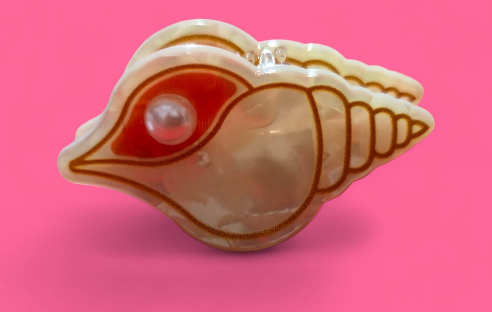 Caja de baratijas con forma de concha de almeja y detalle de perlas, sobre fondo rosa.
