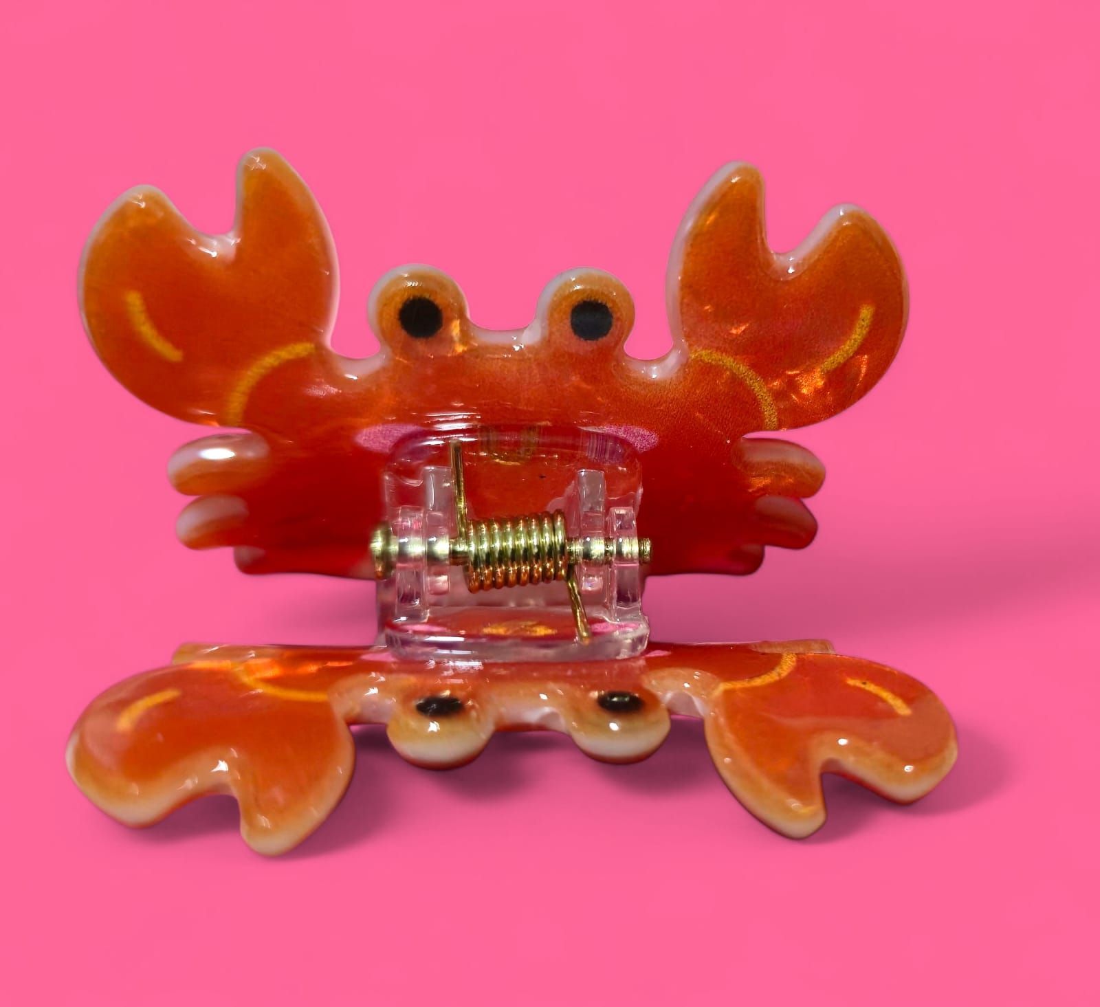 Pinza para el pelo de cangrejo naranja sobre fondo rosa.