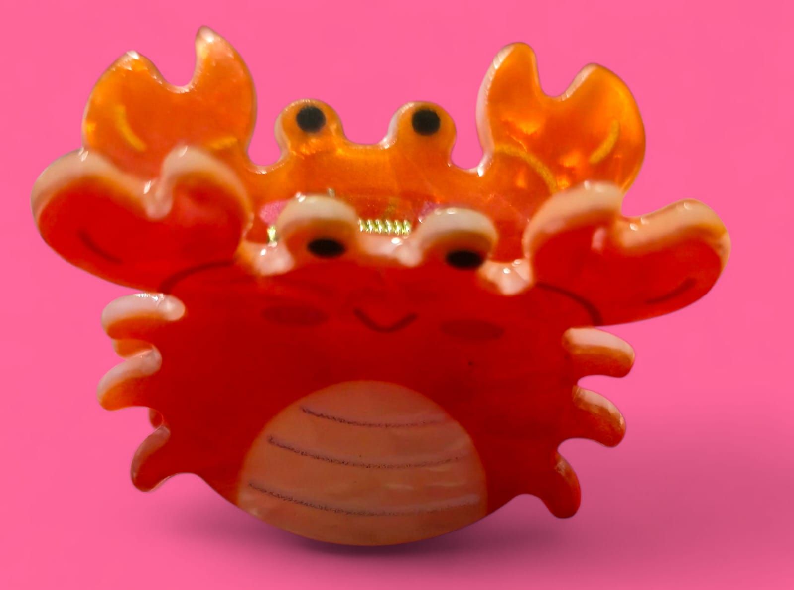 Pinza para el pelo de cangrejo naranja sobre fondo rosa.