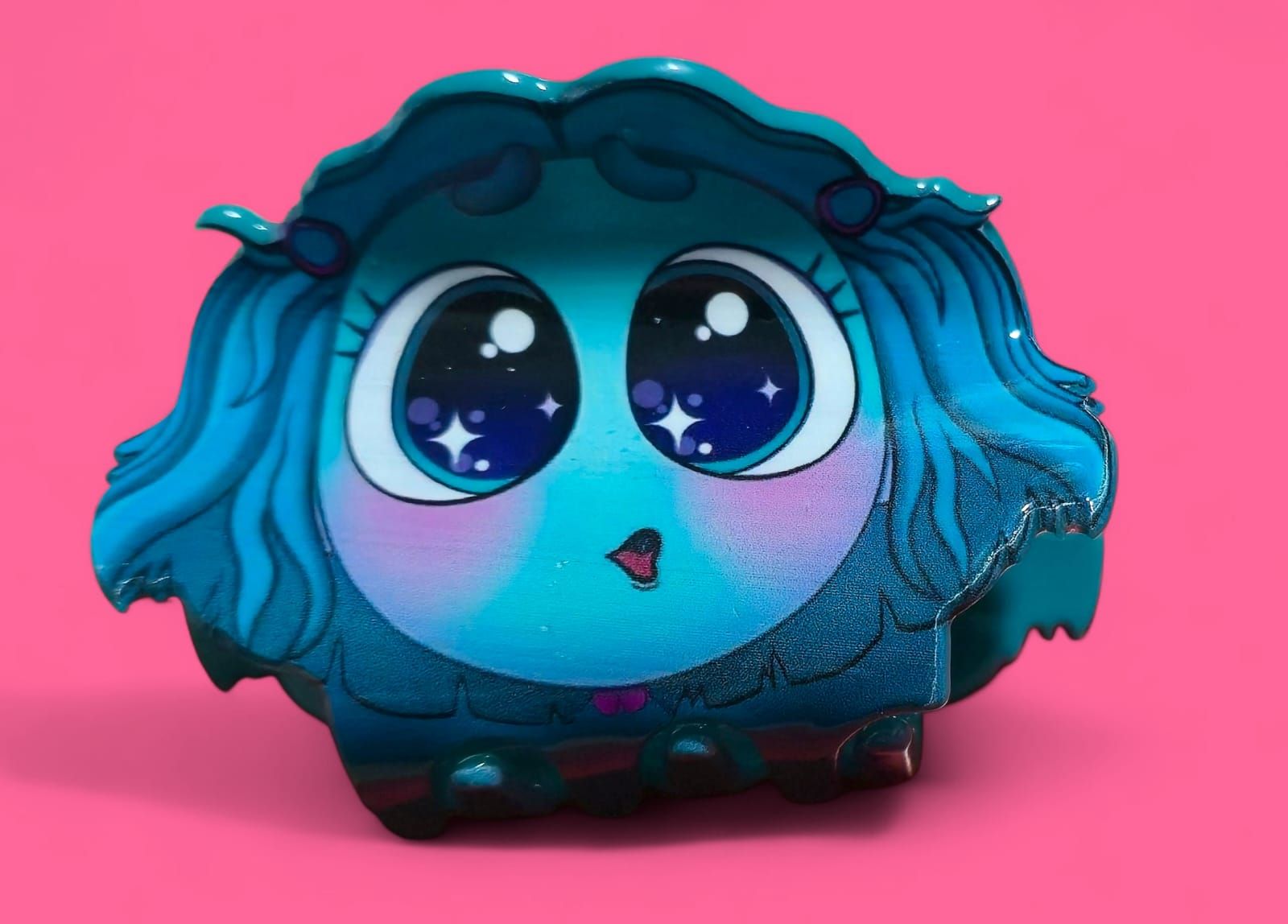 Juguete azul, de forma redonda, con ojos grandes y pelo, sobre un fondo rosa.