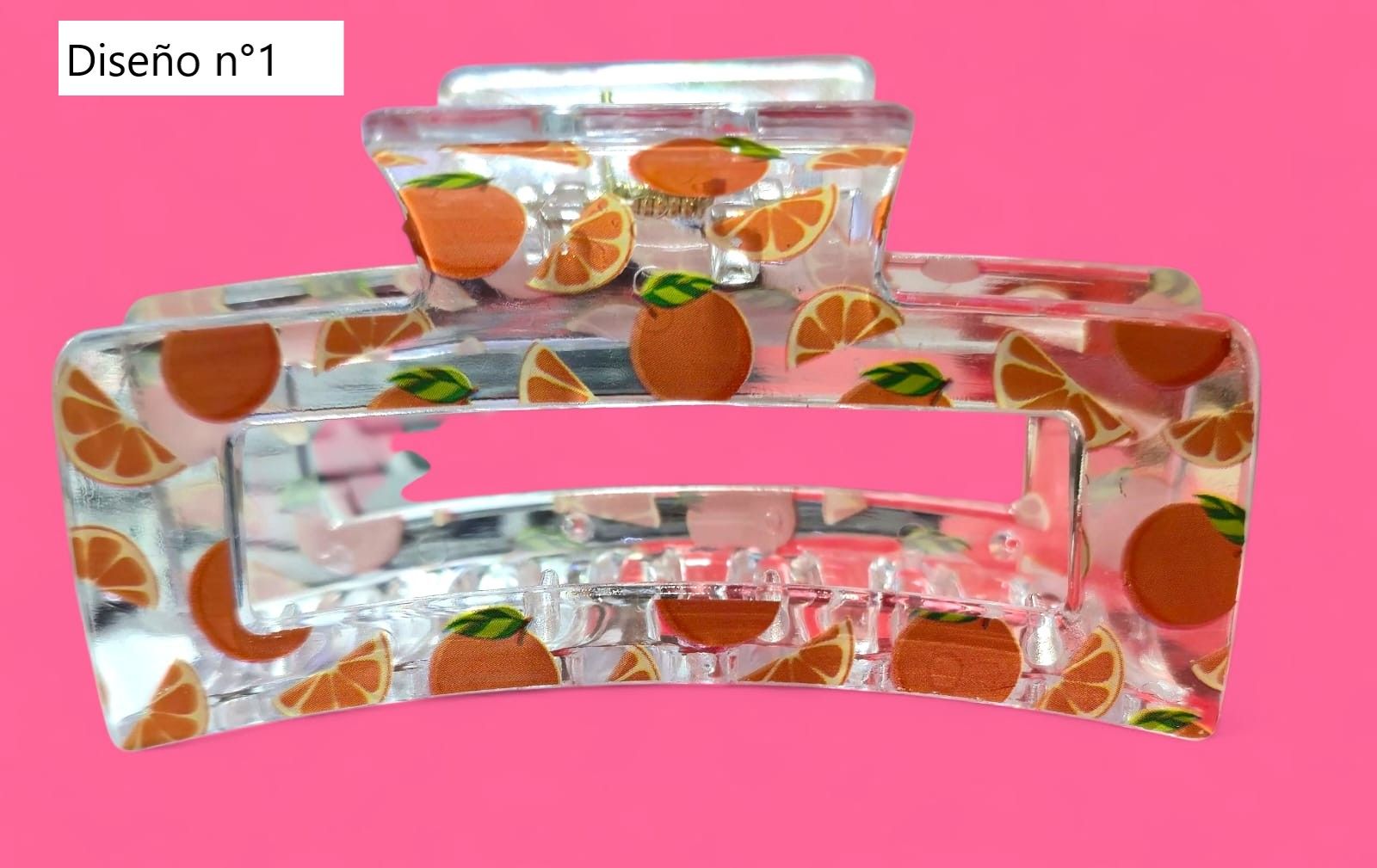 Pinza para el cabello con diseño de fruta naranja sobre fondo rosa.