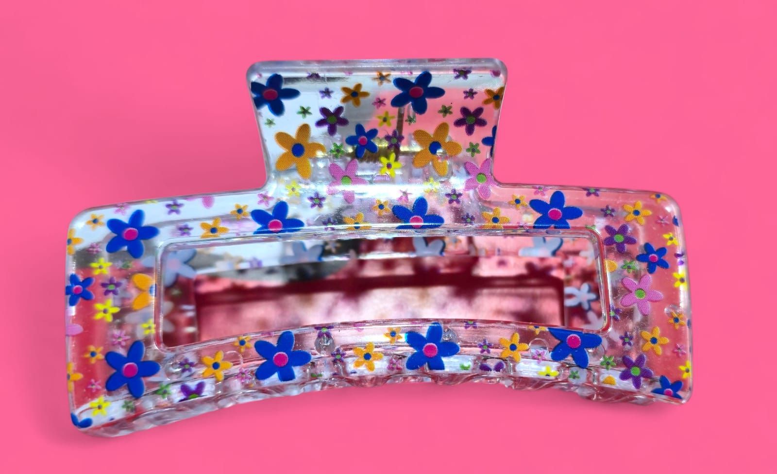 Pinza para el cabello transparente con un colorido estampado floral sobre fondo rosa.