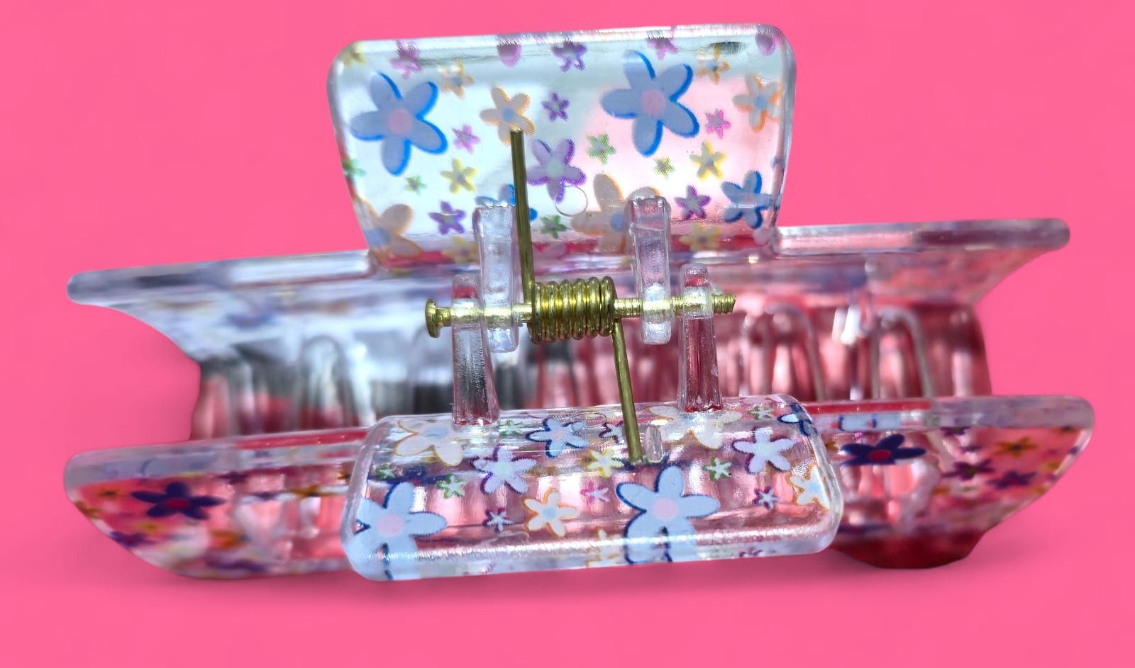 Pinza para el cabello transparente con un colorido estampado floral sobre fondo rosa.
