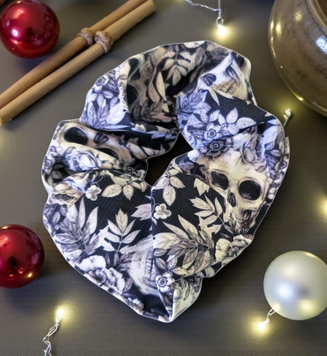 Coletero con estampado floral de calaveras, sobre fondo oscuro, rodeado de adornos y luces navideñas.