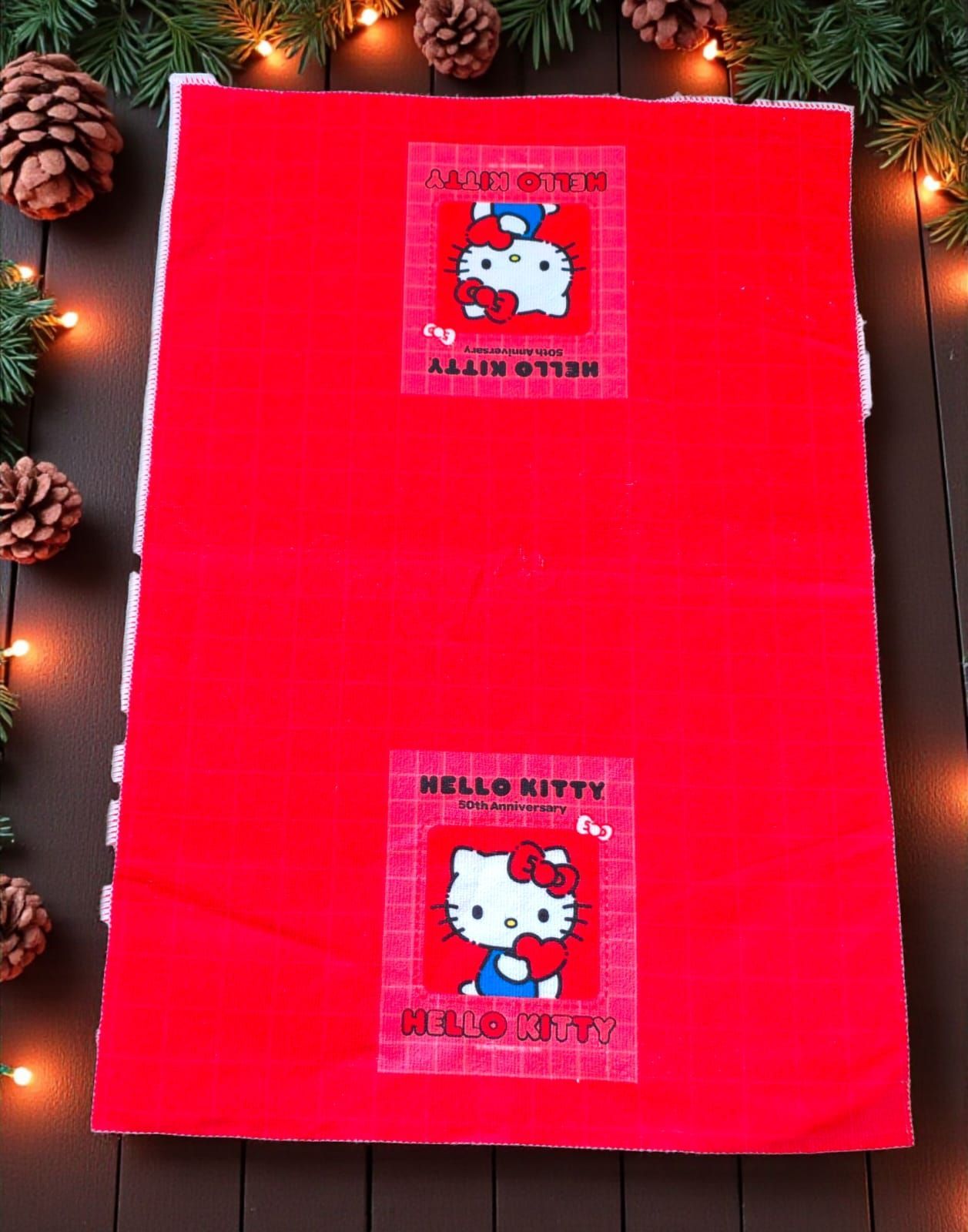 Bolsa de regalo roja con dos pegatinas de Hello Kitty, rodeada de ramas de pino y luces.