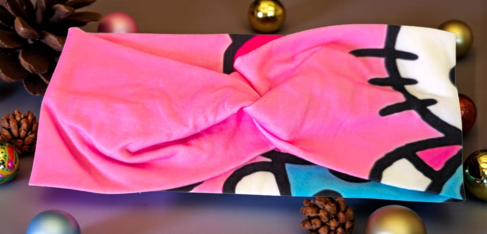 Diadema rosa con estampado, diseño trenzado. Detalles en azul, negro y blanco con adornos navideños.