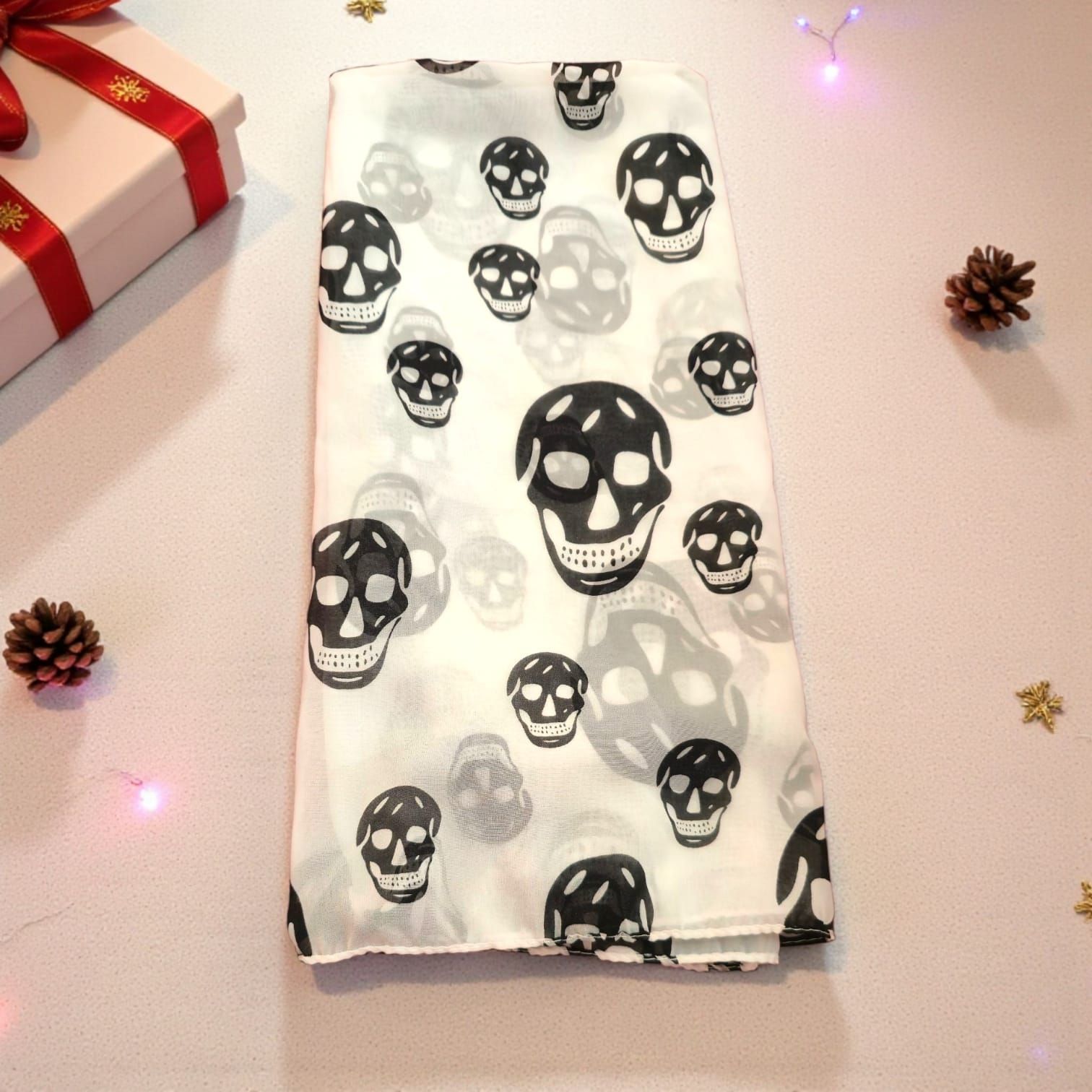 Pañuelo blanco con estampado repetido de calaveras negras, doblado sobre una superficie.