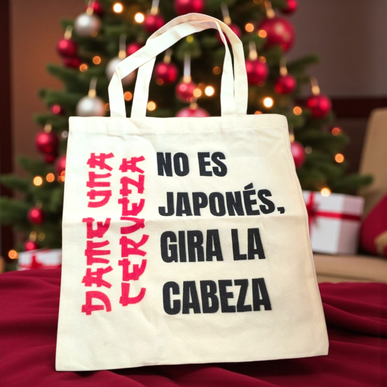 Bolsa de tela color crema con texto en español frente a un árbol de Navidad.