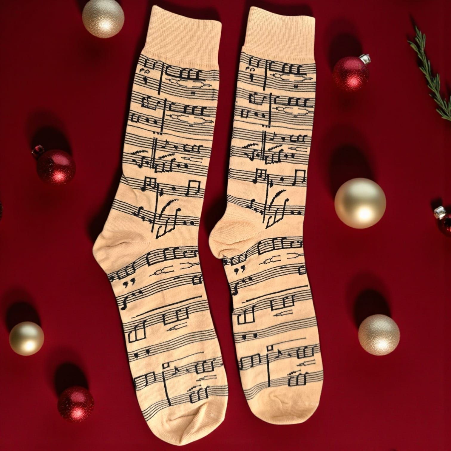 Par de calcetines color beige con diseño de notación musical, sobre fondo rojo con adornos navideños.