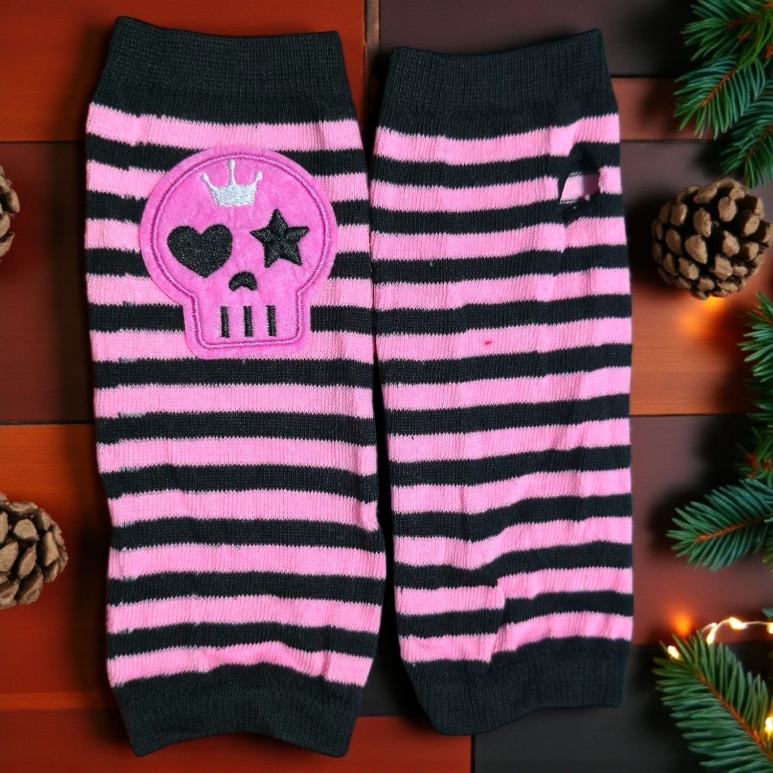 Calentadores de piernas a rayas rosas y negras con aplique de calavera y corona, sobre madera.