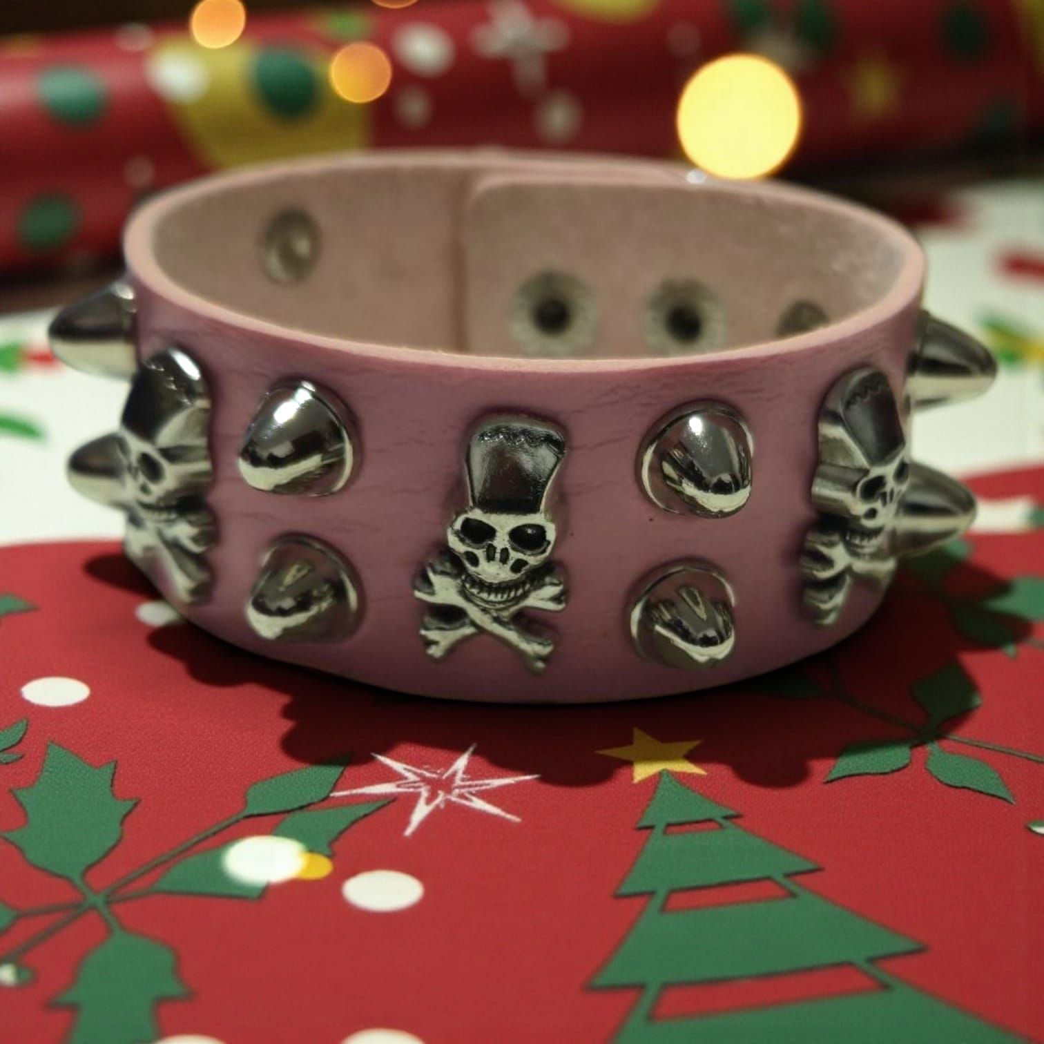 Pulsera de cuero rosa con tachuelas, calaveras y detalles de pinchos, envuelta en papel de regalo navideño.