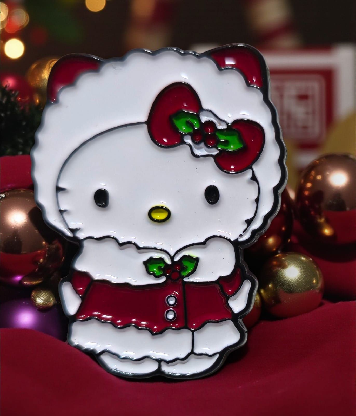 Hello Kitty con un abrigo navideño rojo y blanco, con un lazo de acebo, sobre un fondo de adornos navideños.