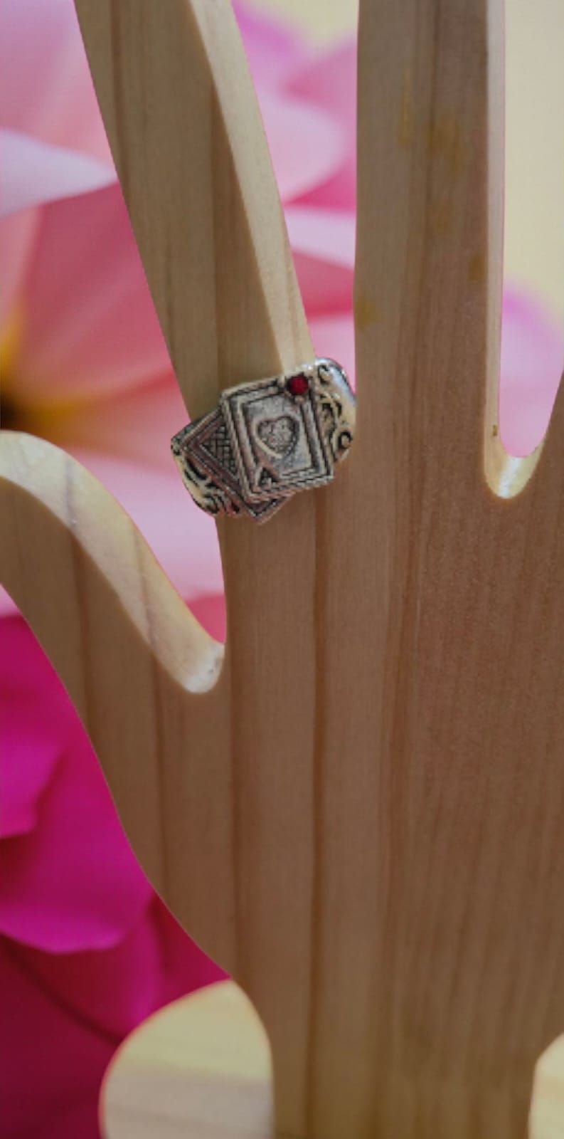 Un anillo con diseños de cartas de juego sobre un soporte de madera con forma de mano, sobre un fondo de flores rosas.
