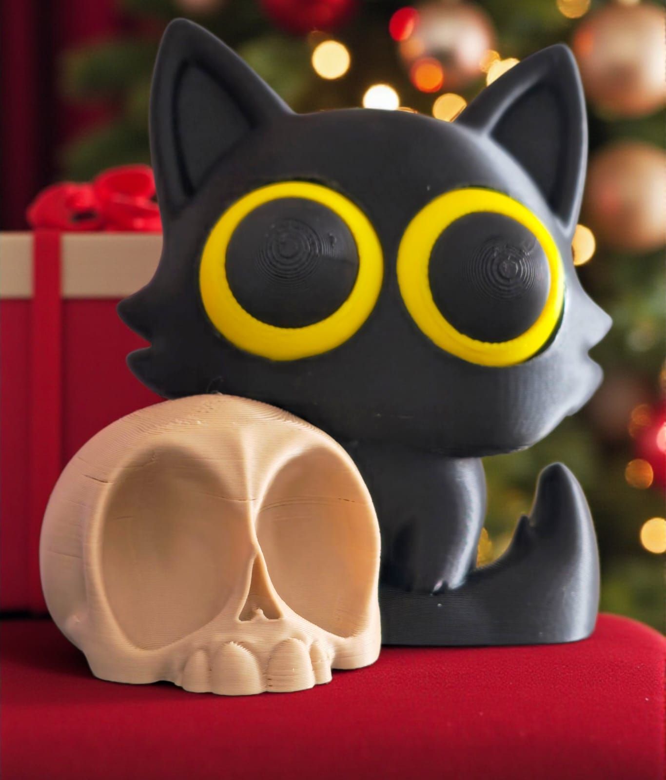 Figura de gato negro con grandes ojos amarillos y cráneo marrón claro sobre fondo rojo. Árbol de Navidad al fondo.