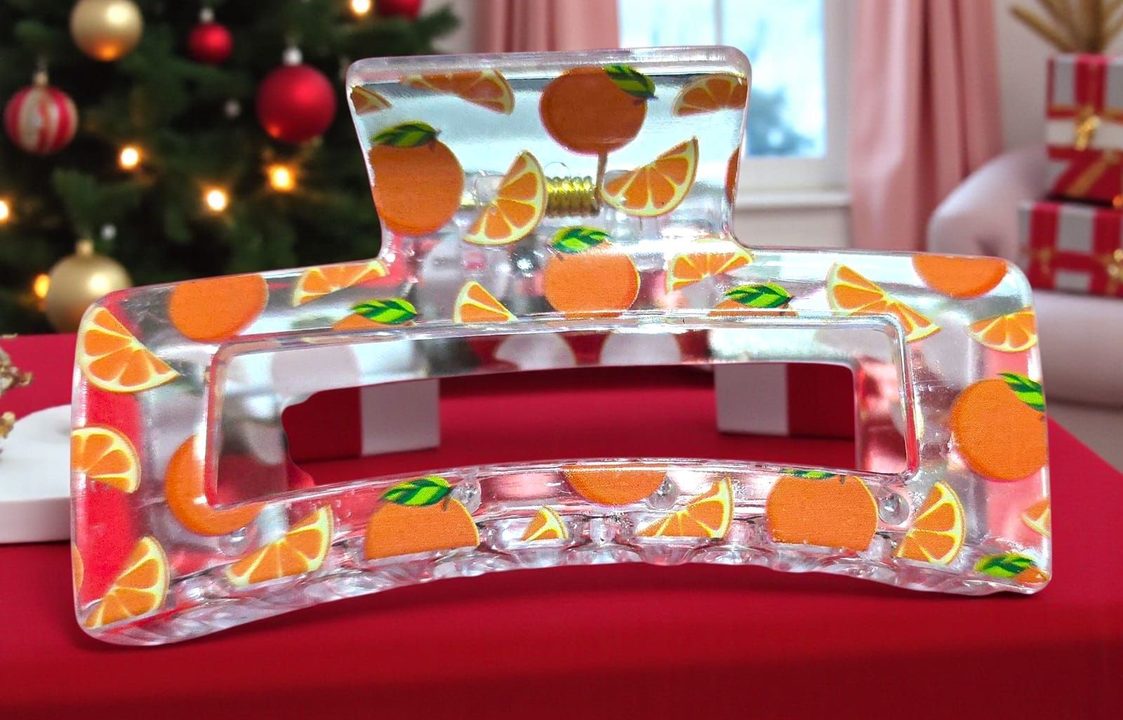 Pinza para el cabello transparente con rodajas de naranja incrustadas, sobre una superficie roja.