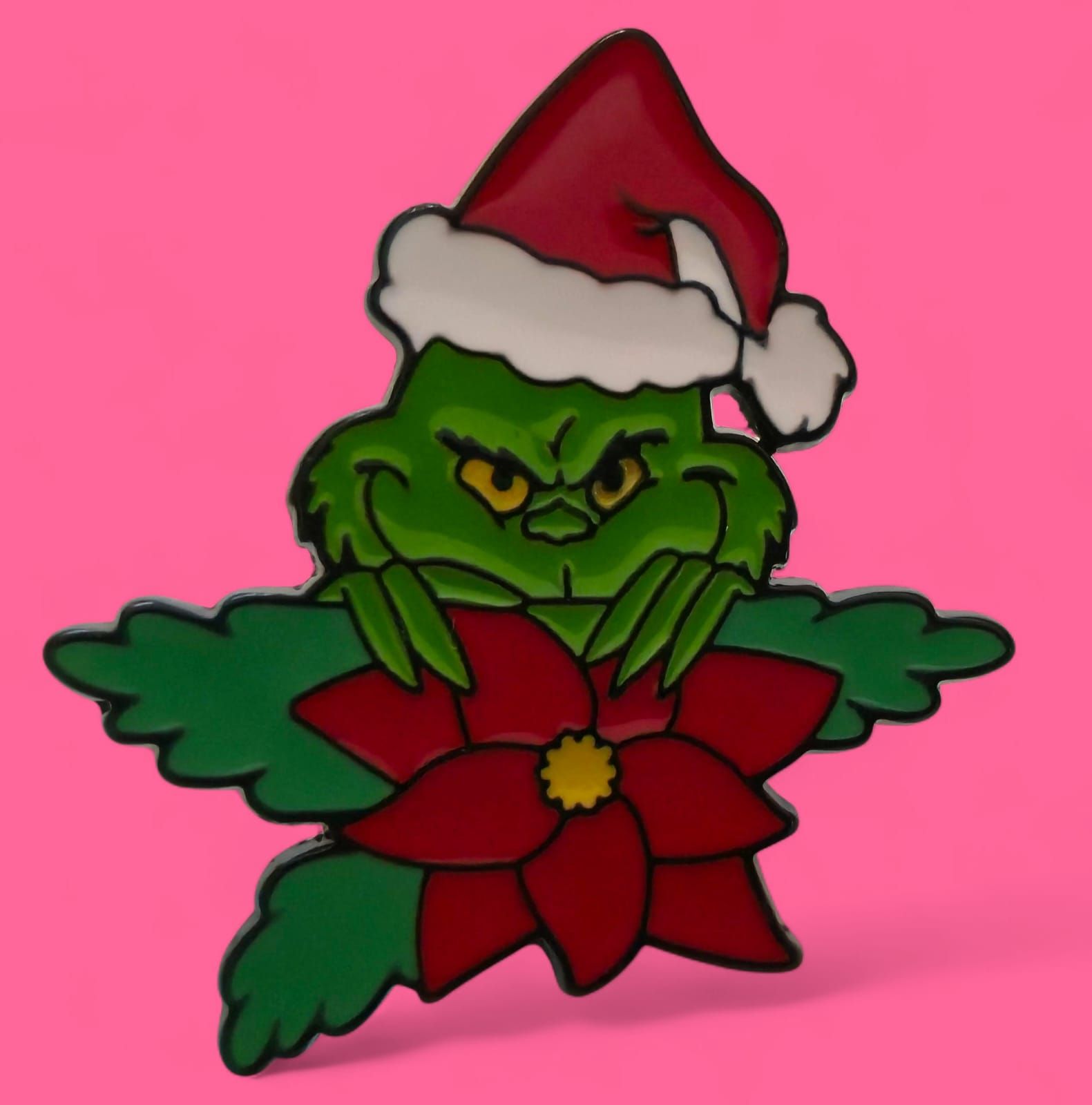 El Grinch, con gorro de Papá Noel, asomándose por encima de una flor de Pascua. Cara verde con expresión traviesa.