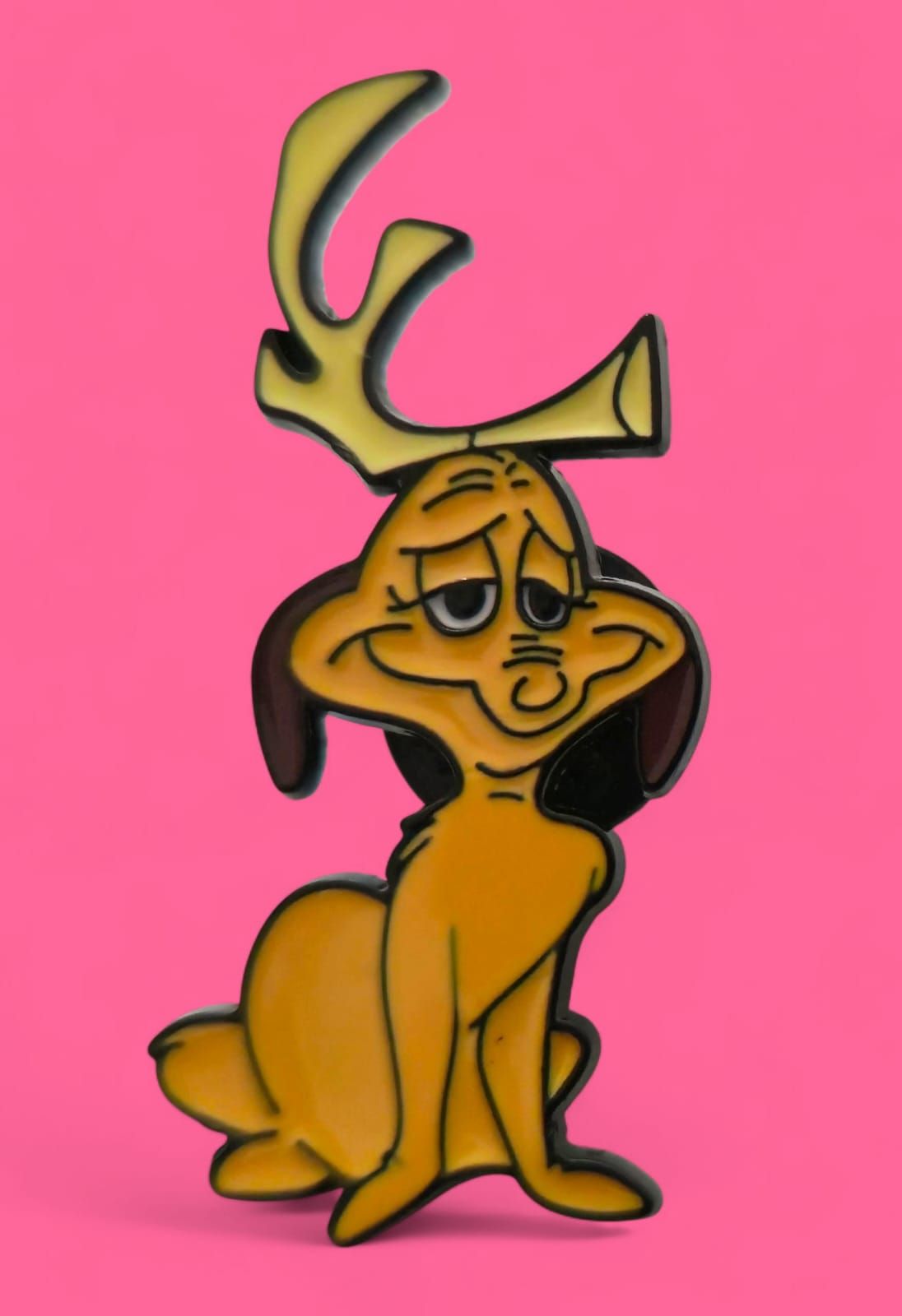 Personaje amarillo de Sam-I-Am con cuernos parecidos a astas, sentado, detalles marrones, sobre fondo rosa.