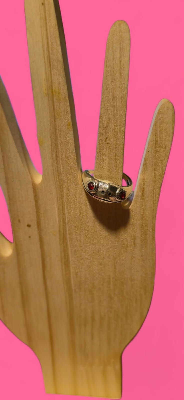 Anillo con piedras oscuras sobre una mano de madera con fondo rosa.