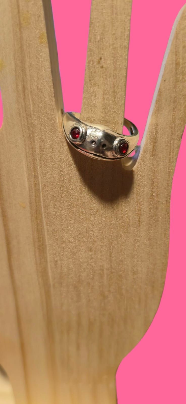 Anillo con piedras oscuras sobre una mano de madera con fondo rosa.
