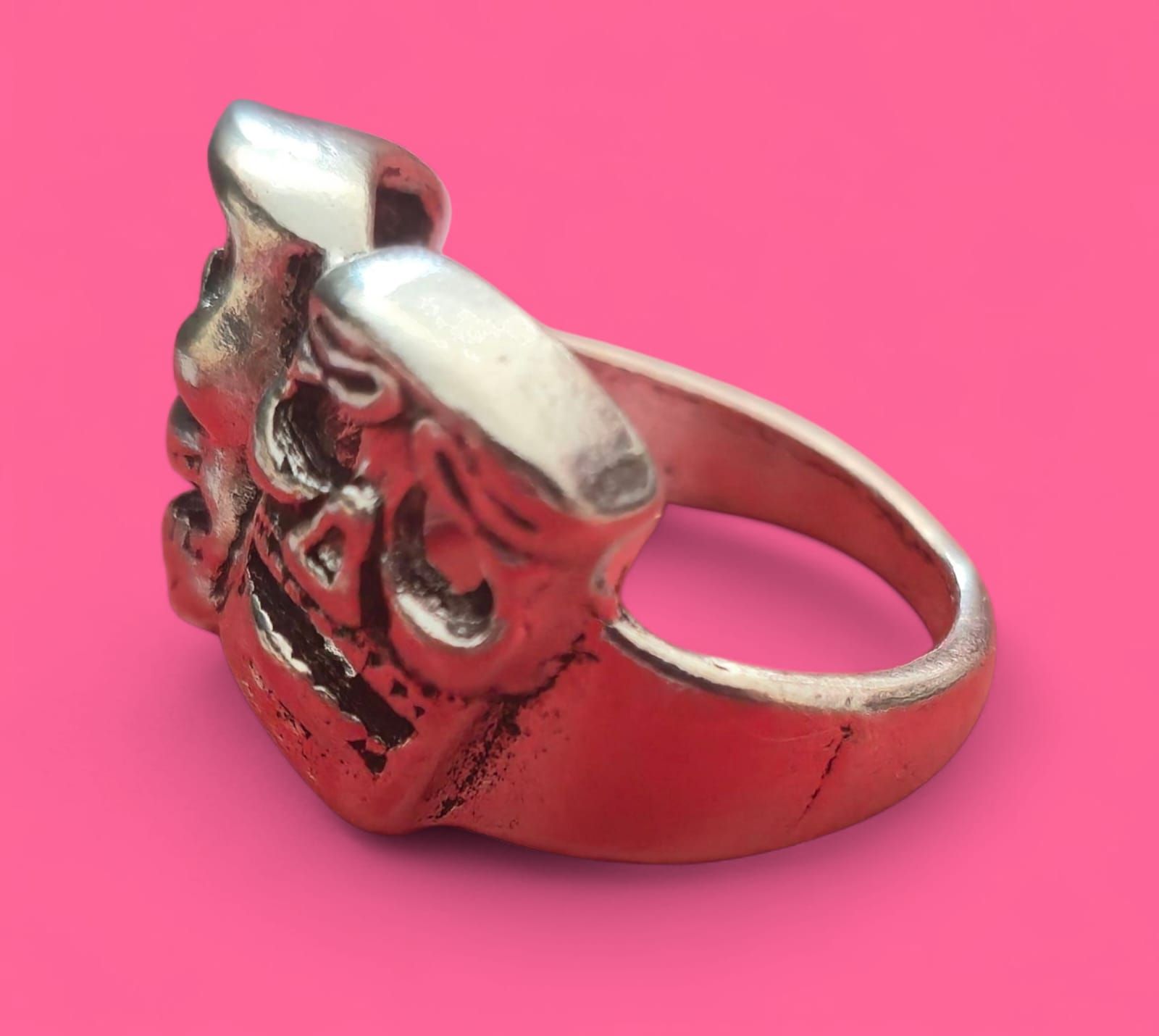 Anillo de plata con una cara decorativa sobre fondo rosa.