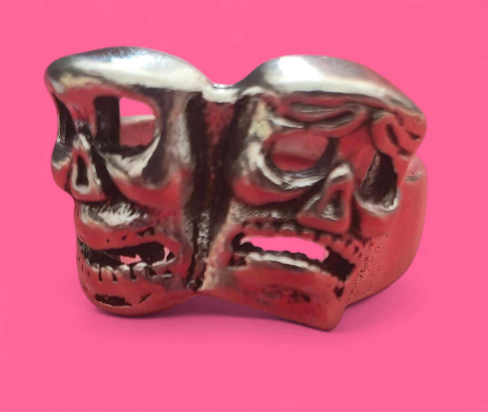 Anillo de plata con una cara decorativa sobre fondo rosa.
