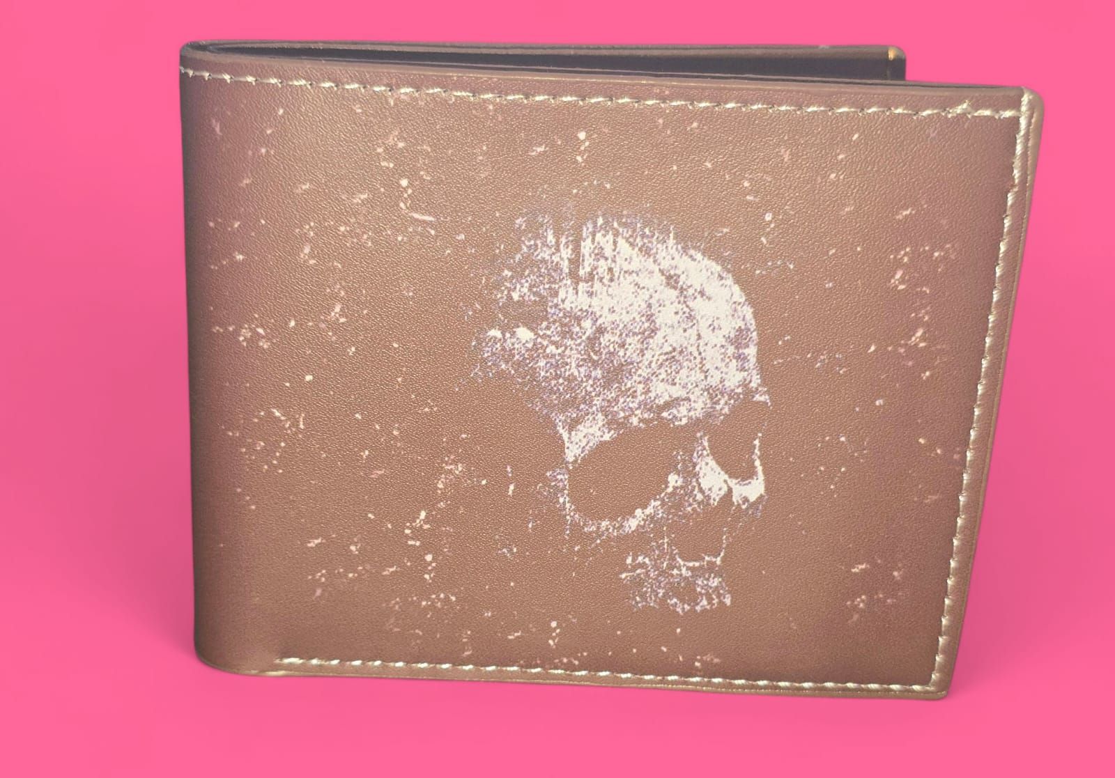 Cartera de piel marrón con un diseño de calavera blanca sobre fondo rosa.