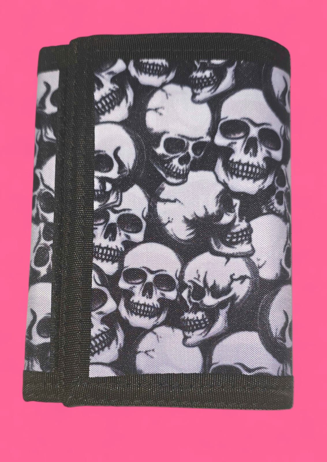Cartera con estampado de calaveras en blanco y negro, cerrada, sobre fondo rosa.