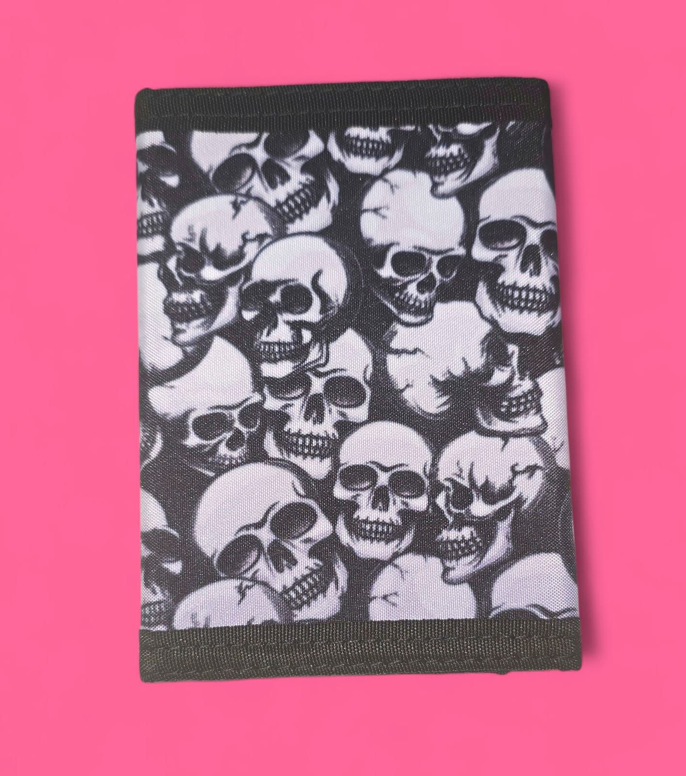 Cartera con estampado de calaveras en blanco y negro, cerrada, sobre fondo rosa.