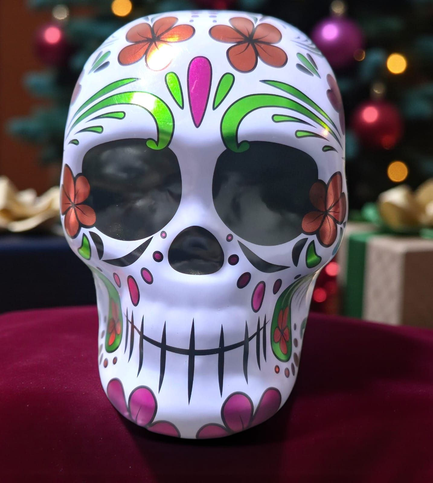 Calavera de azúcar decorada con flores naranjas y rosas, delante de un árbol de Navidad.