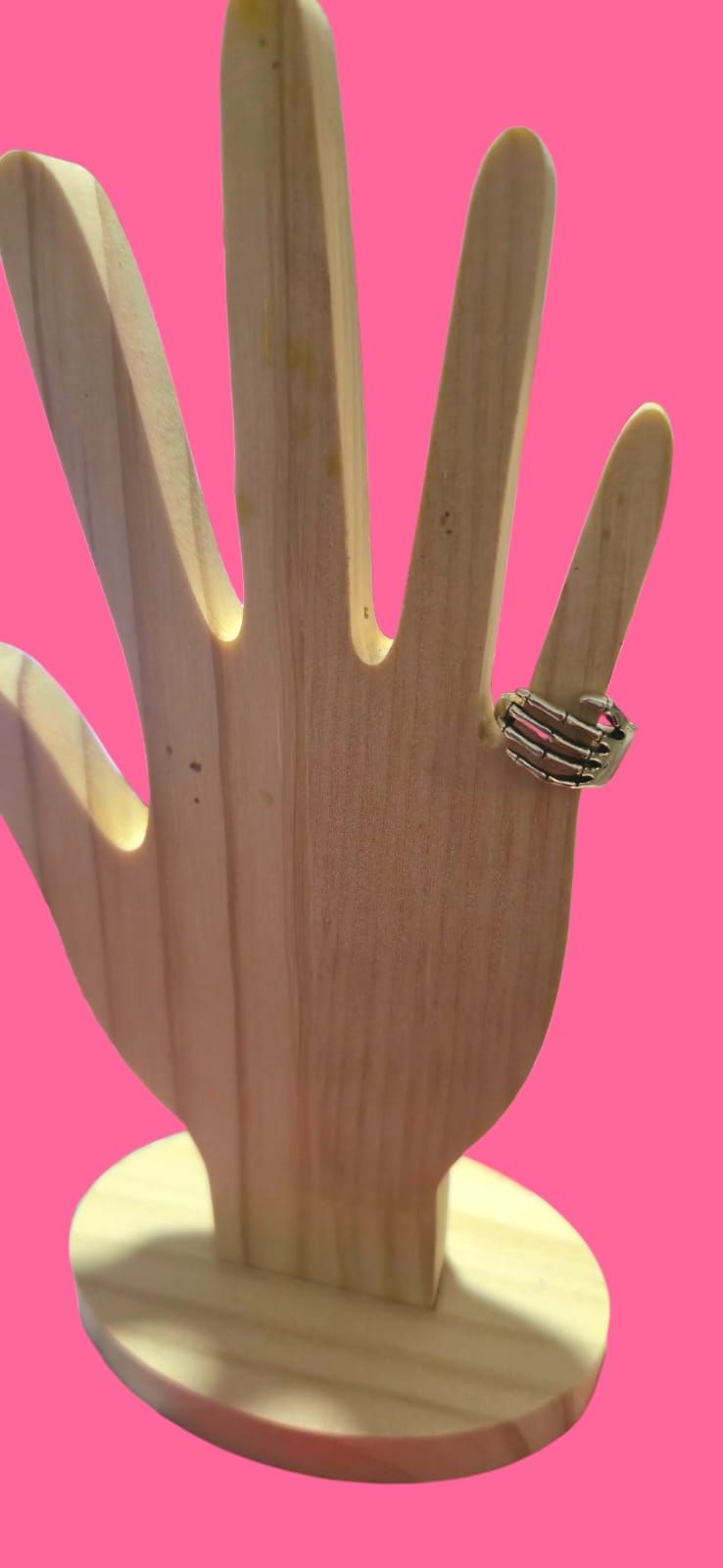 Un anillo de plata sobre una mano de madera contra un fondo rosa brillante.