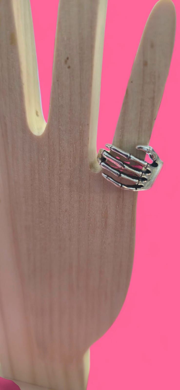 Un anillo de plata sobre una mano de madera contra un fondo rosa brillante.