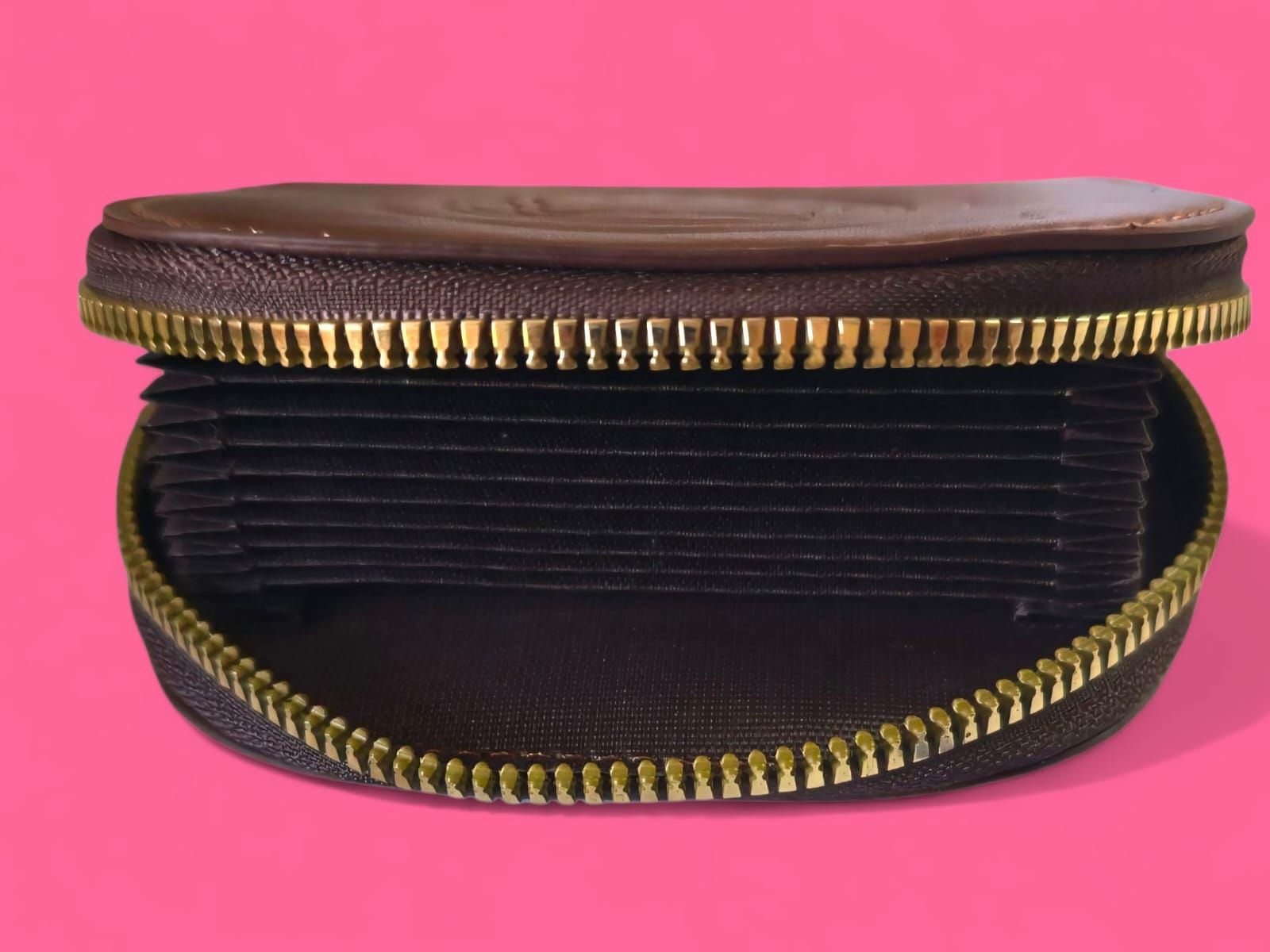 Monedero de piel marrón con cremallera dorada y logotipo grabado, sobre fondo rosa.