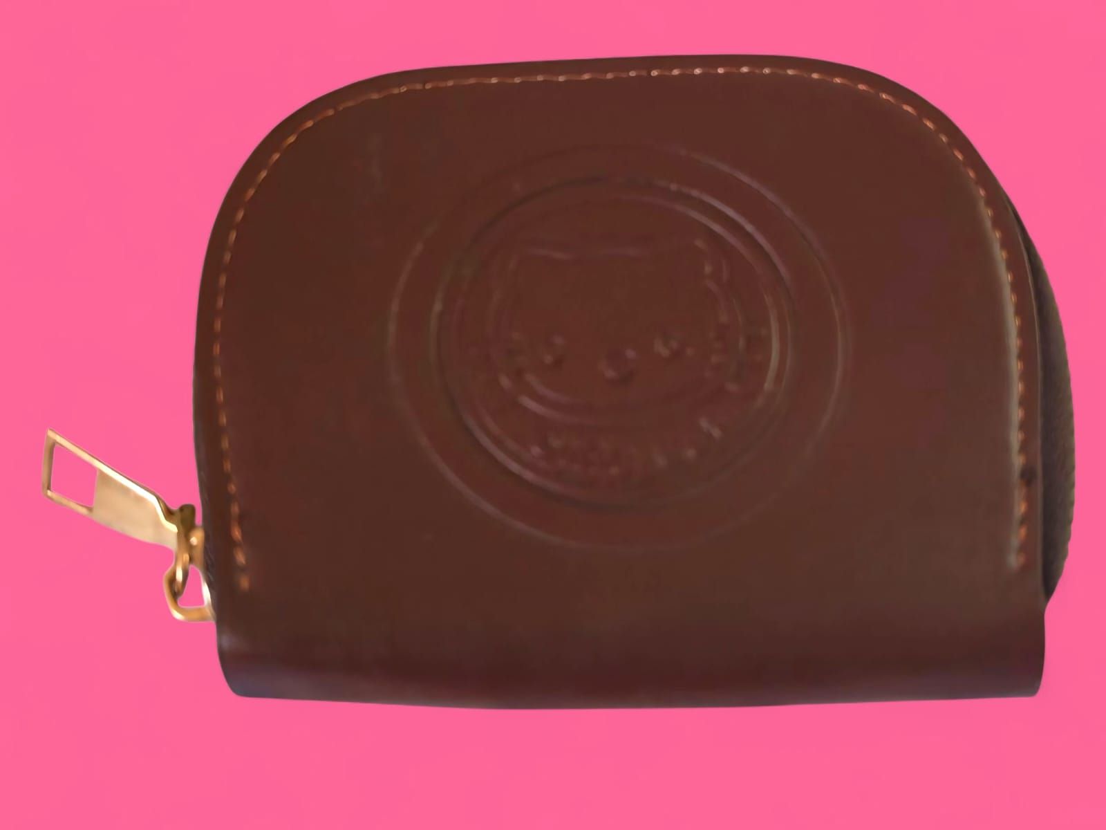 Monedero de piel marrón con cremallera dorada y logotipo grabado, sobre fondo rosa.