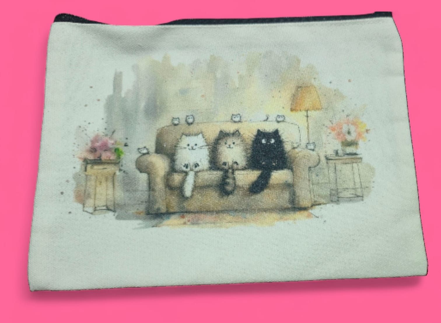 Bolsa de lona con gatos de acuarela sobre un sofá, con una lámpara y flores, sobre un fondo rosa.