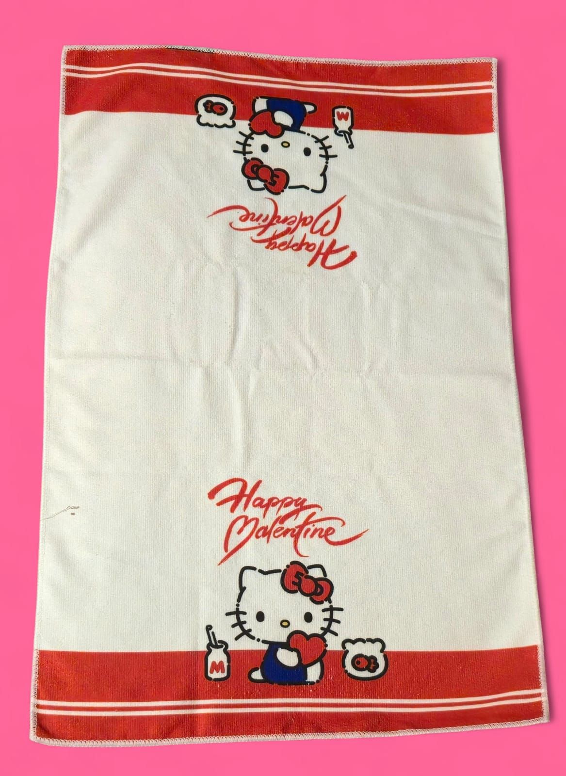 Toalla blanca de Hello Kitty para el Día de San Valentín con rayas rojas y texto; dibujo de Kitty con corazones y regalos.