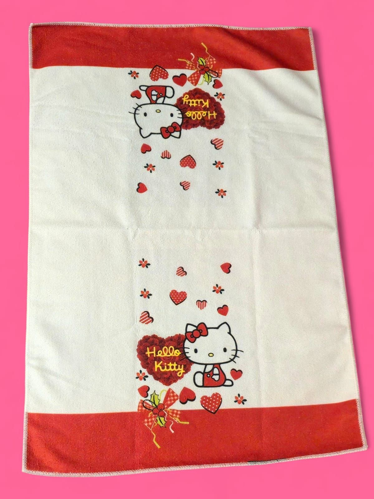 Toalla de Hello Kitty con detalles rojos, corazones y texto sobre fondo blanco.