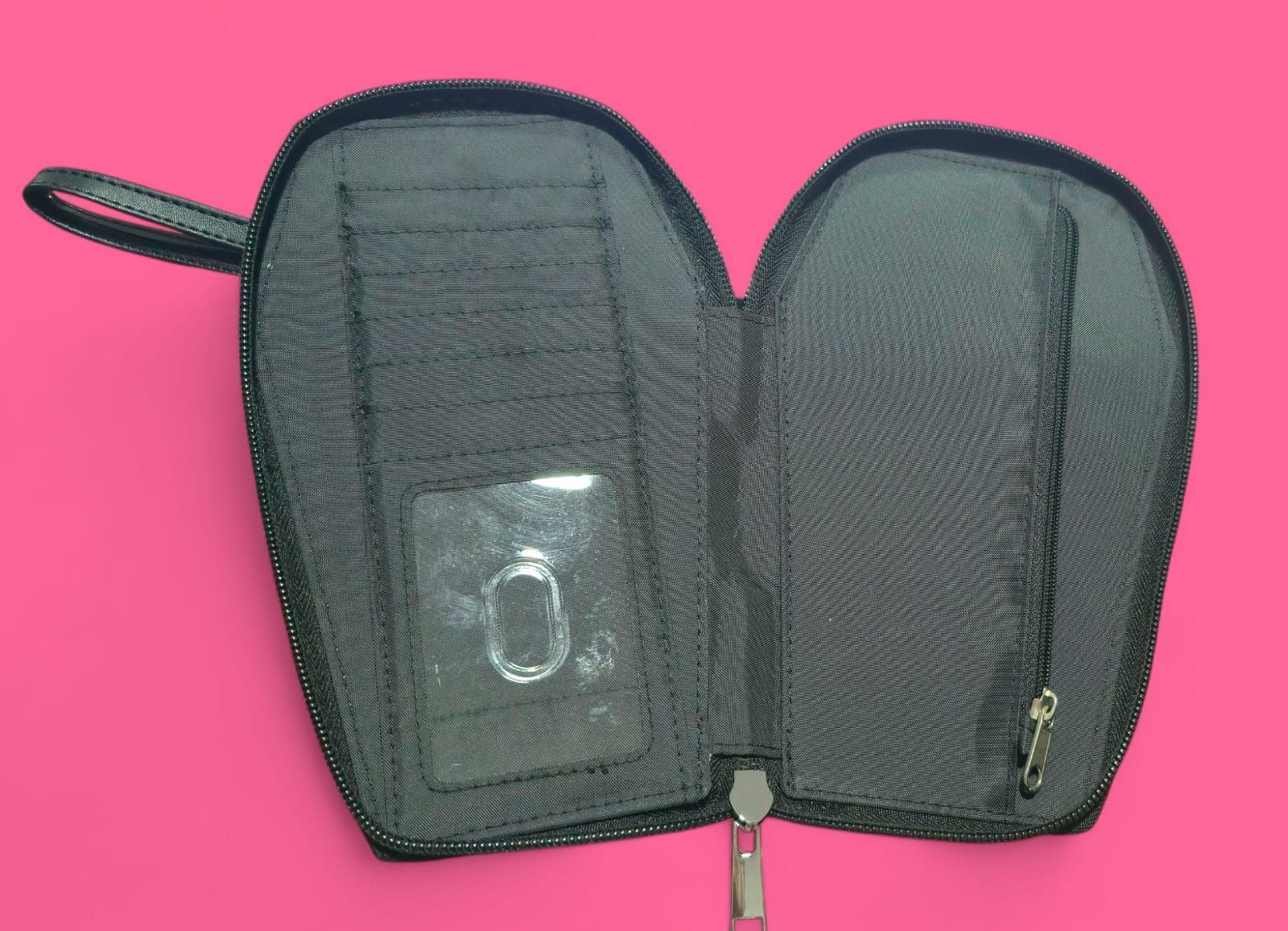 Cartera negra con forma de ataúd, diseño floral azul y correa de muñeca sobre fondo rosa.