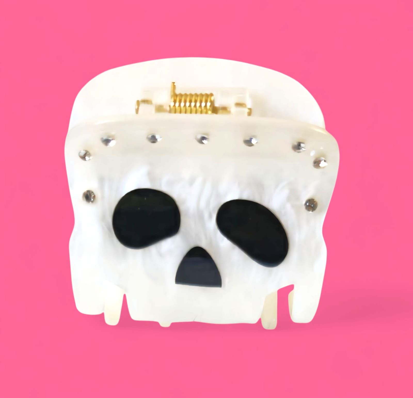 Pinza para el pelo blanca con forma de calavera, con cuencas negras para los ojos y la nariz, pedrería y bisagra dorada.