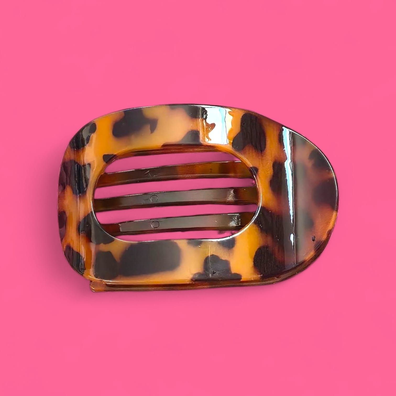 Pinza para el cabello con estampado de carey sobre fondo rosa, de forma ovalada con listones horizontales.