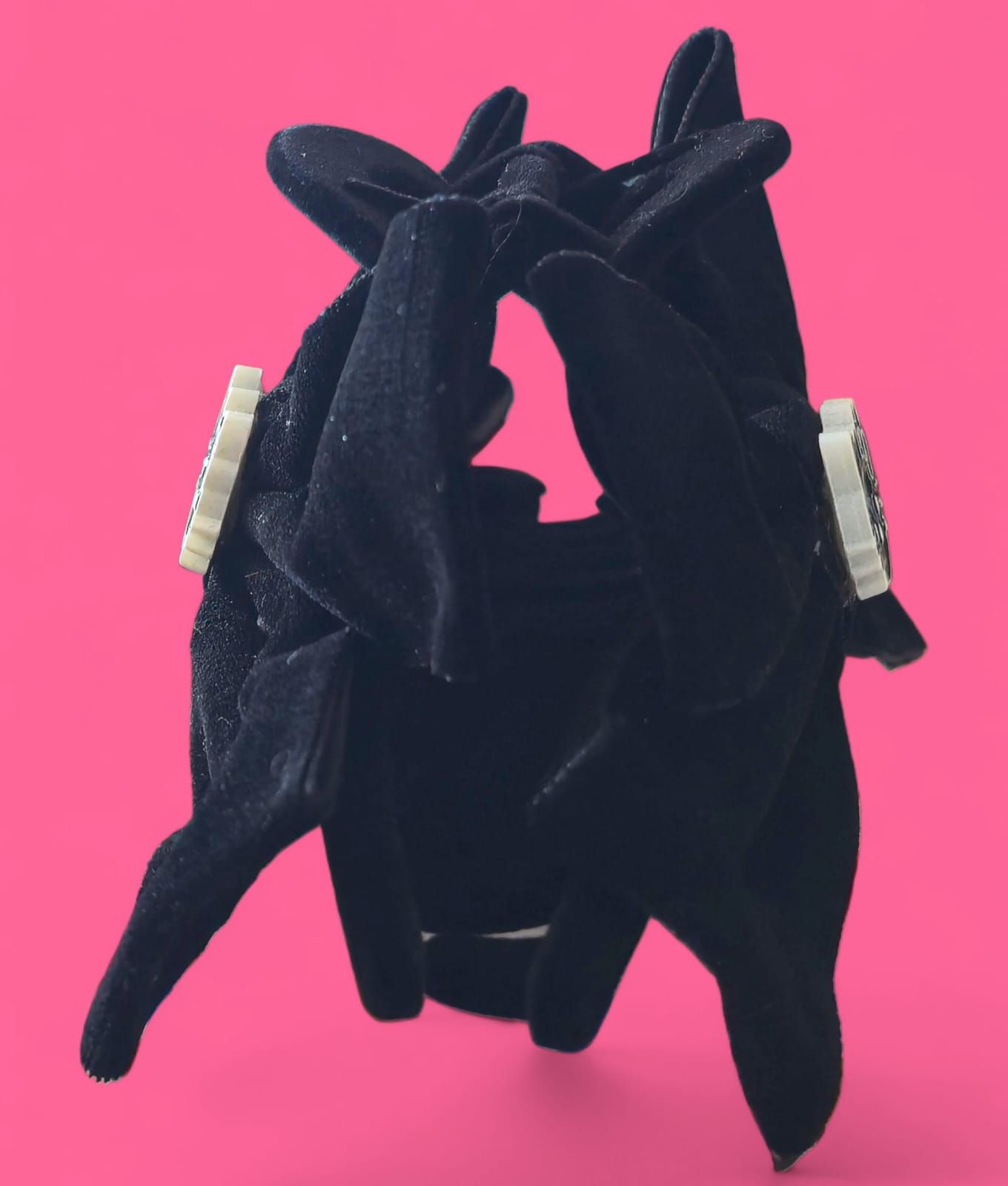 Pinza para el pelo con lazo de terciopelo negro y adorno de Hello Kitty sobre fondo rosa.