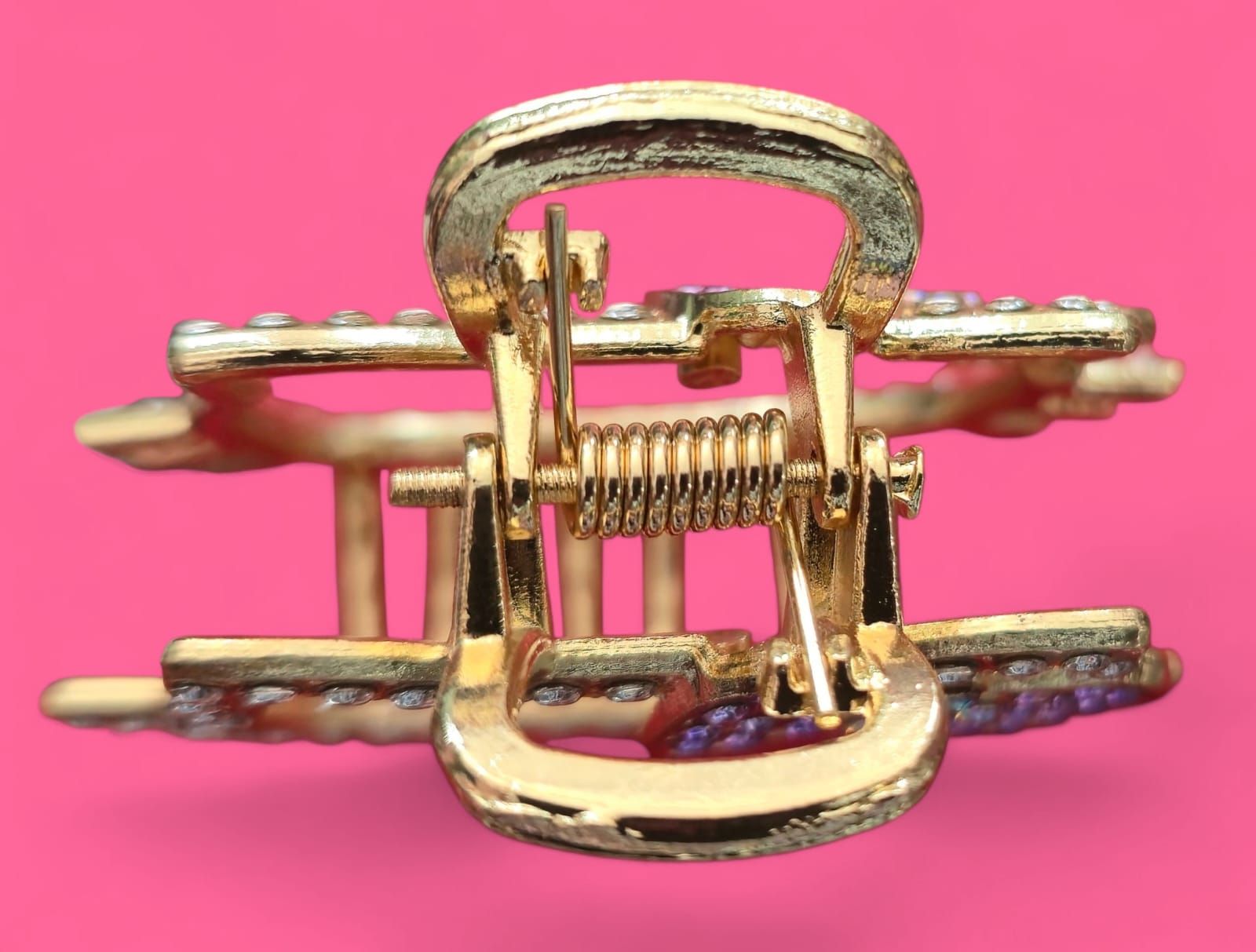 Pinza para el pelo Hello Kitty dorada con brillantes morados y transparentes sobre fondo rosa.