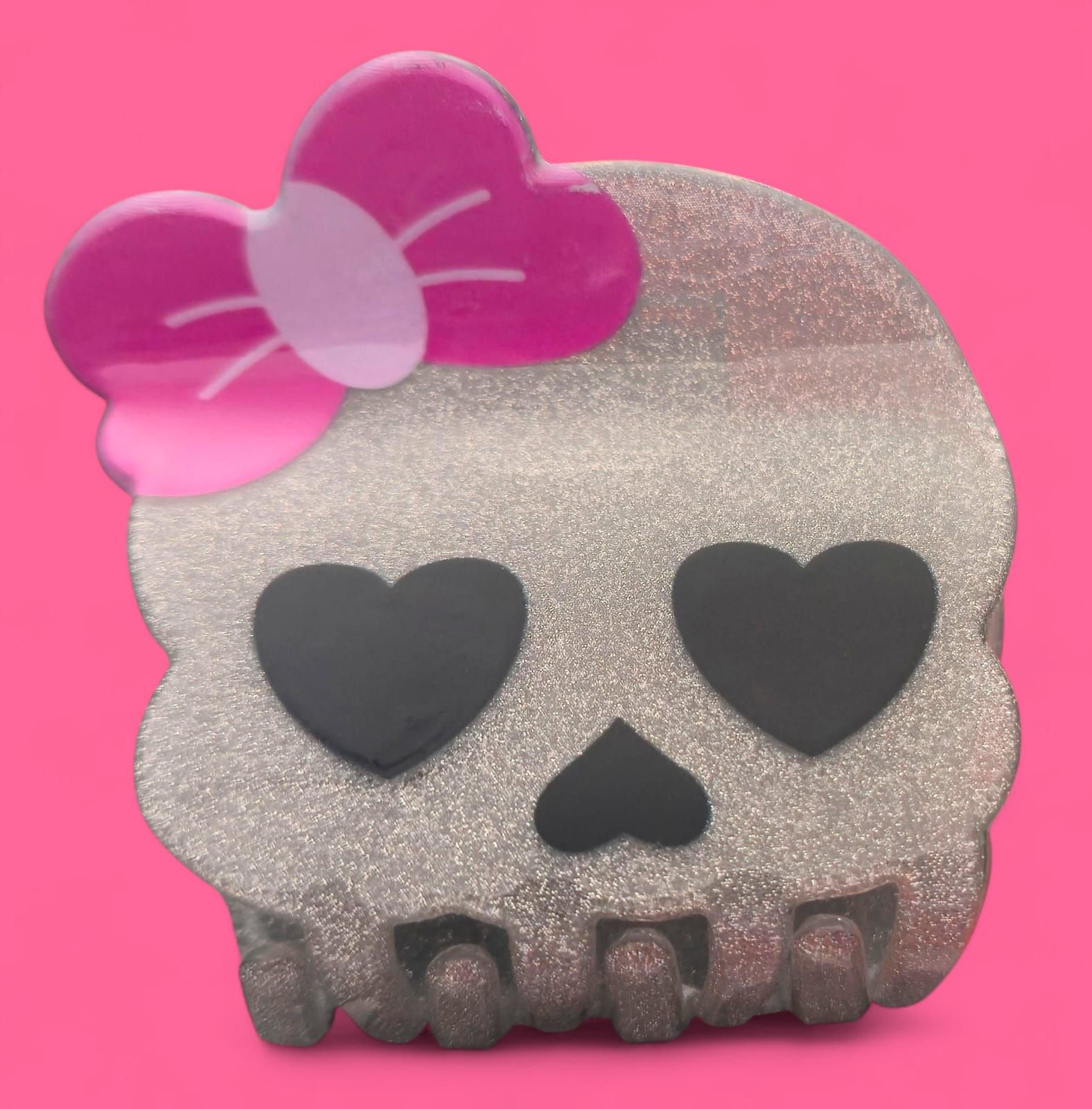 Calavera brillante con ojos en forma de corazón y un lazo rosa, sobre un fondo rosa.