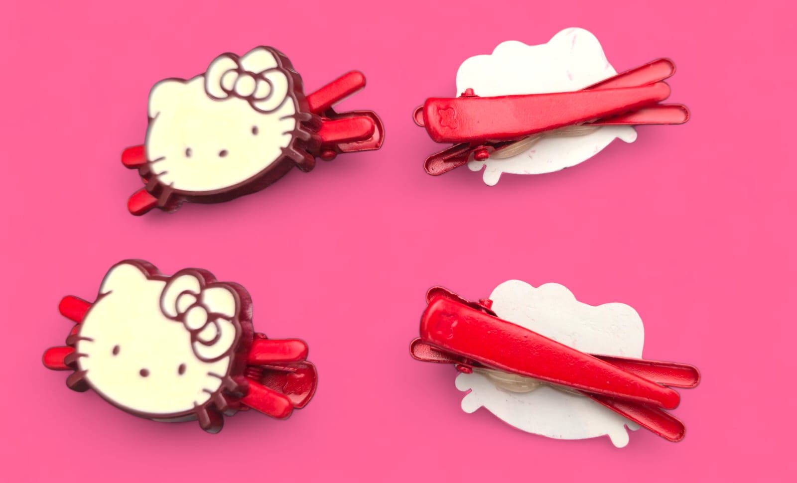 Cuatro pinzas para el pelo de Hello Kitty rojas y blancas sobre un fondo rosa.