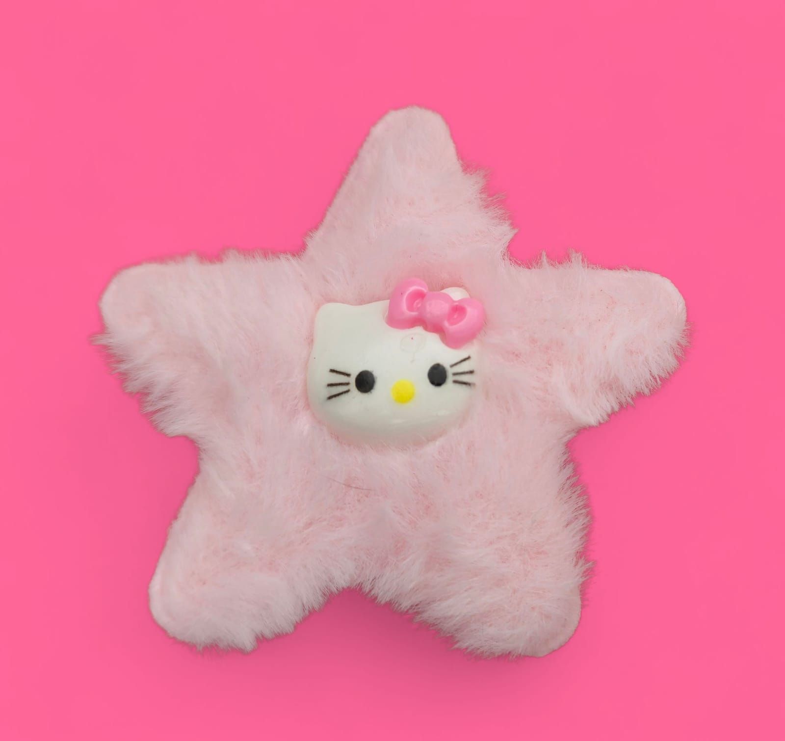 Peluche rosa en forma de estrella con la cara de Hello Kitty sobre fondo rosa.