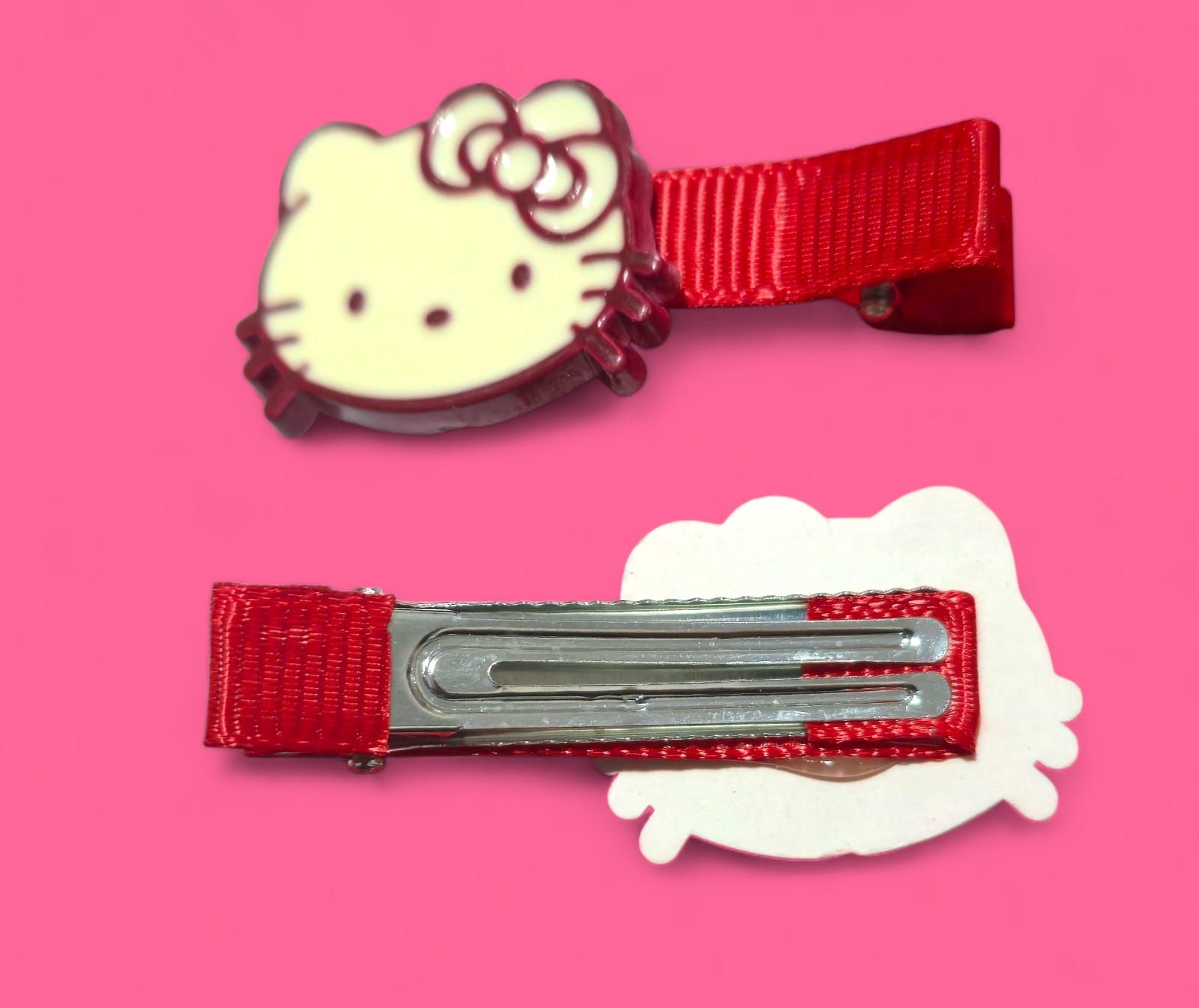 Dos pinzas para el pelo de Hello Kitty, cinta roja, fondo rosa.