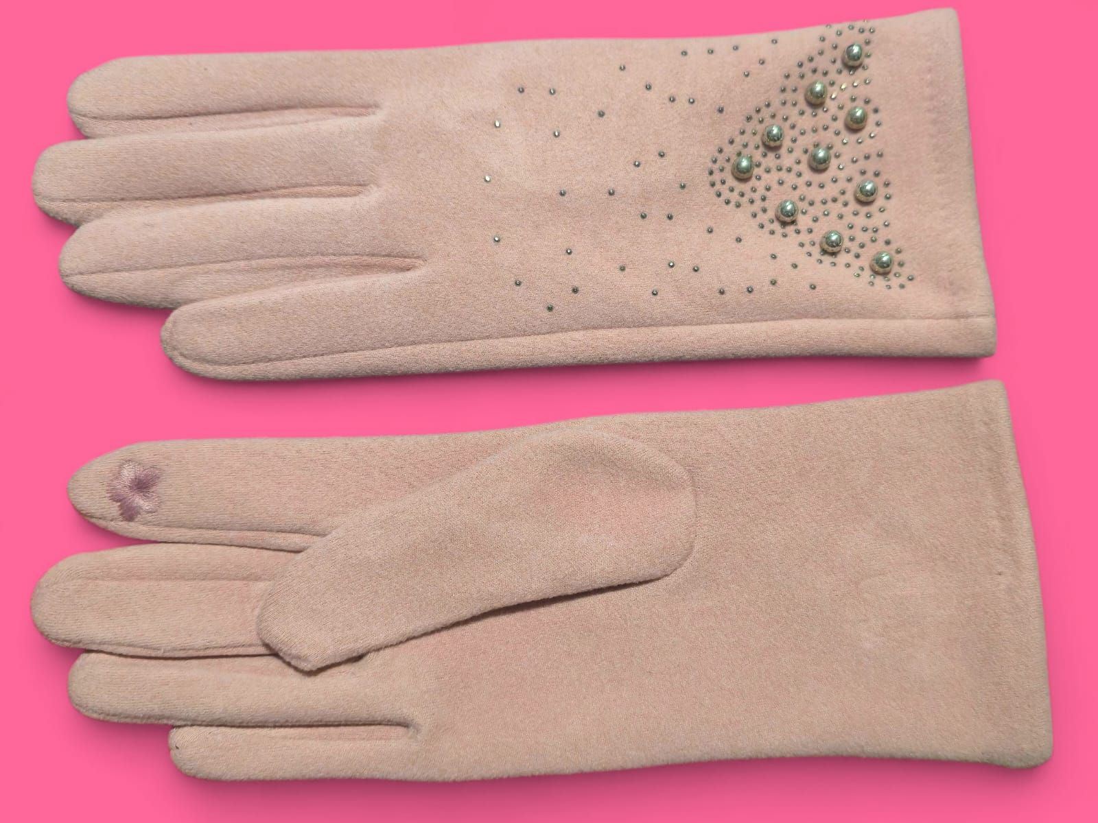Guantes de ante rosa con adornos de cuentas sobre fondo rosa.